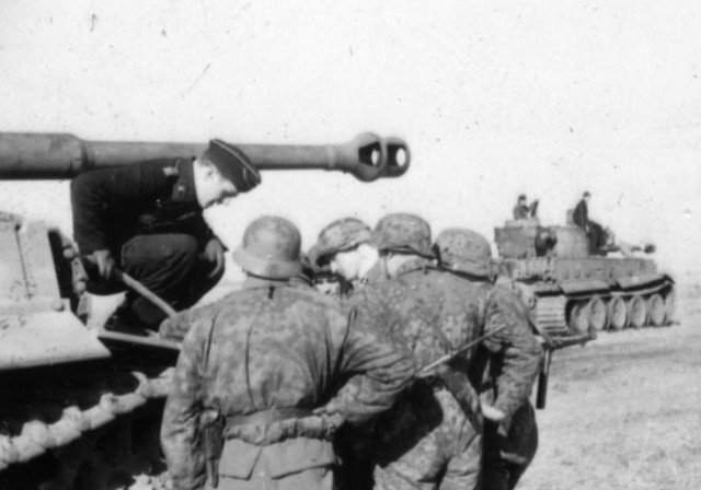 Waffen SS soldiers having a discussion with a Panzer Mk VI Tiger commander. – By Bundesarchiv – CC BY-SA 3.0