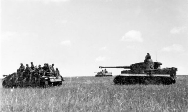 Waffen SS soldiers on a Stug, followed by two Panzer MK VI Tiger tanks drive to the startline of operation Citadel – By Bundesarchiv – CC BY-SA 3.0