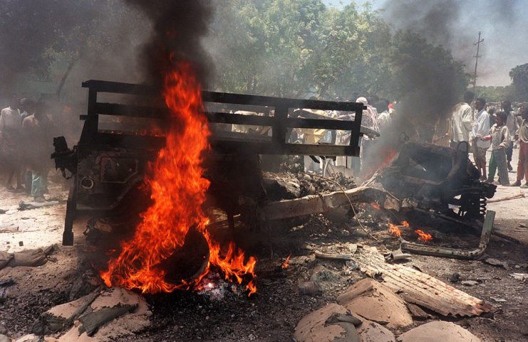 Somali people standing around a burning Jeep