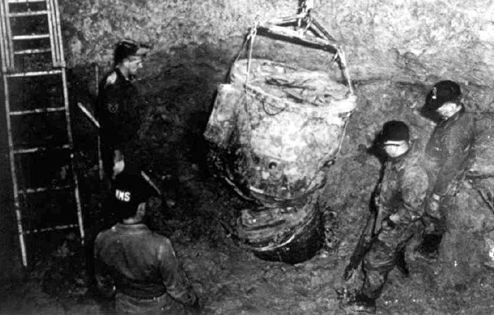 Four crew members standing around a Mark 39 thermonuclear bomb buried in the ground