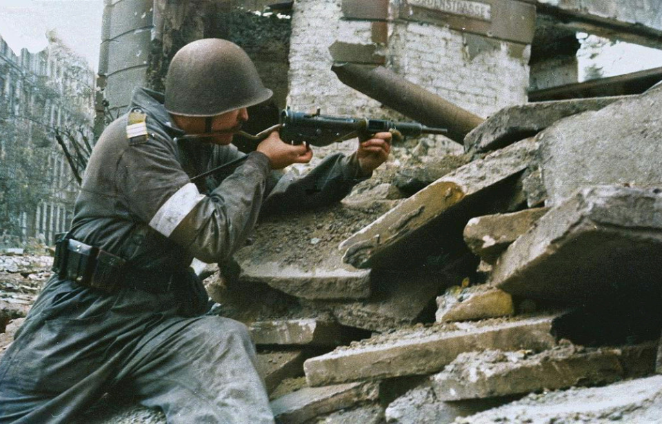 Member of the Polish Home Army aiming a rifle through an open spot in a damaged building