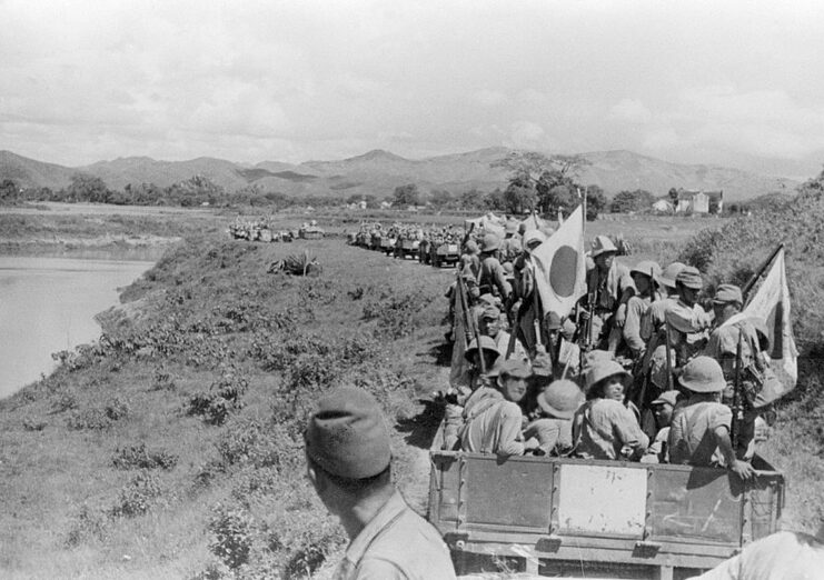 Japanese soldiers riding in vehicles driving along a river-side road