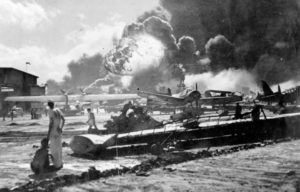 Sailors standing around aircraft, watching an explosion in the distance