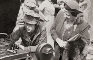 Queen Elizabeth II tinkering with a car engine while Elizabeth the Queen Mother watches