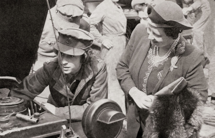 Queen Elizabeth II tinkering with a car engine while Elizabeth the Queen Mother watches