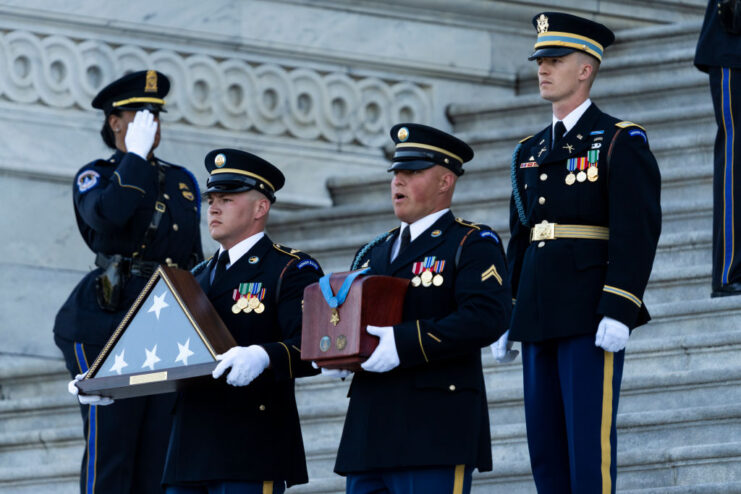 Members of a US military honor guard walking down the steps of the US Capitol with a folded American flag and an urn containing Ralph Puckett's ashes