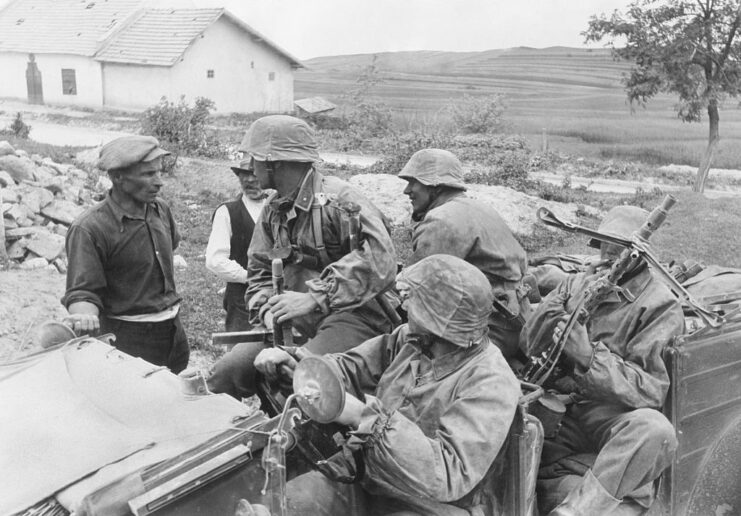 Waffen-SS troops sitting in a military vehicle, speaking with two Ukrainian men