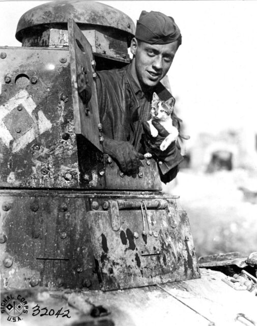 Sgt. Paul Postal holding Mustard the cat while poking out of a tank turret
