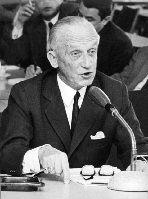 Hasso von Manteuffel sitting at a table, which has a microphone on top of it