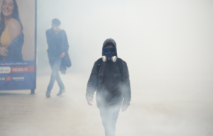 Person walking through smoke in gas mask.