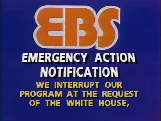 Emergency Broadcast System (EBS) warning, reading, "EBS / EMERGENCY ACTION NOTIFICATION / WE INTERRUPT OUR PROGRAM AT THE REQUEST OF THE WHITE HOUSE,"