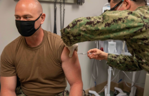 A male sailor administering the COVID-19 vaccine on another sailor