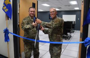 US Air Force Brig. Gen. Charles McDaniel and Col. Chance Geray using large scissors to cut a blue ribbon