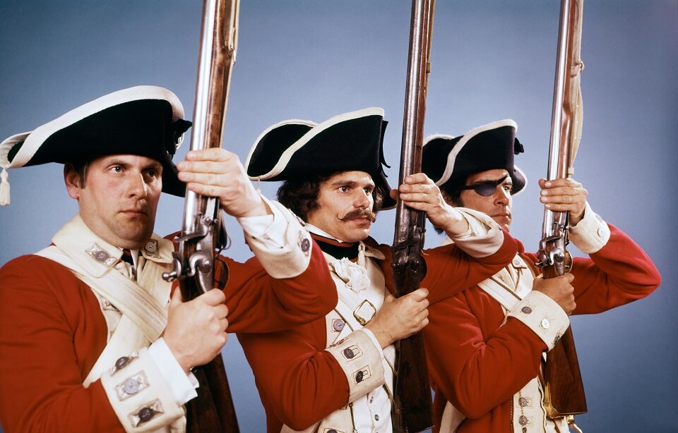 Three men wearing British soldier uniforms and holding muskets.