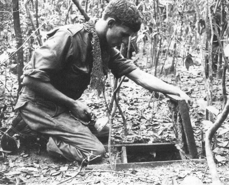 Australian soldier kneeling down in front of an entrance to one of the Viet Cong's tunnels