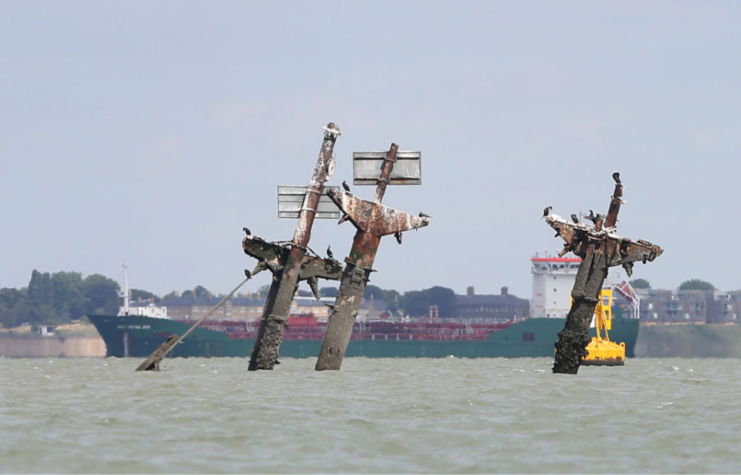 Freighter sailing behind the three masts of the sunken SS Richard Montgomery