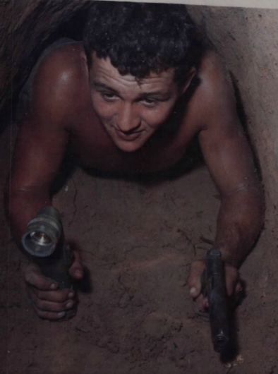 Sgt. Ronald A. Payne crawling through a Viet Cong tunnel while holding a flashlight and an M1911 pistol