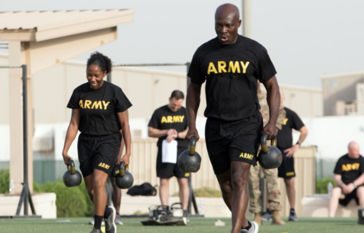 Two US Army soldiers carrying weights across a field