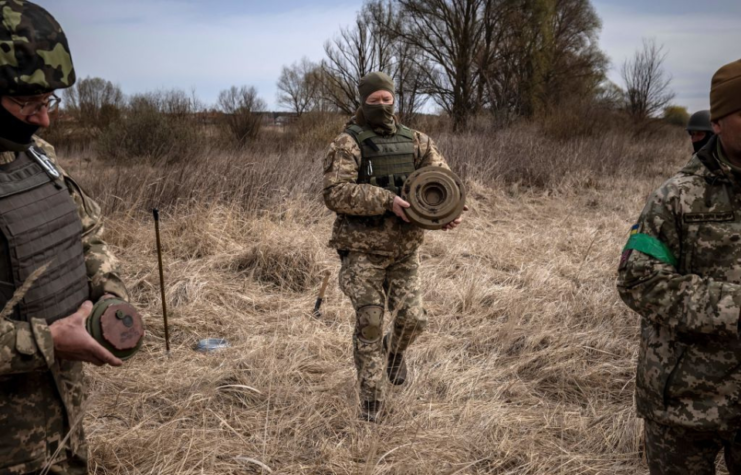 Three men in camouflage clearing land mines from a field