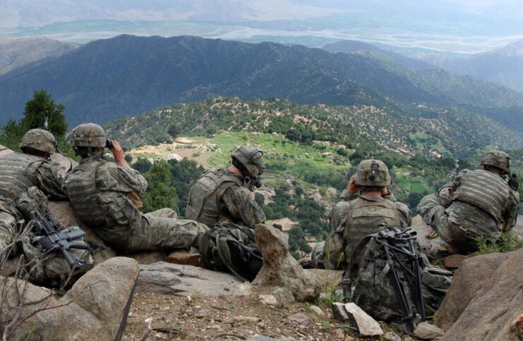 Five US Army soldiers looking through bincoulars while sitting on a ridge