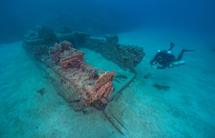 Diver swimming near a rusty military vehicle