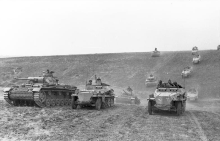 Panzerkampfwagen IIIs and light-armored half-track vehicles driving down a hill