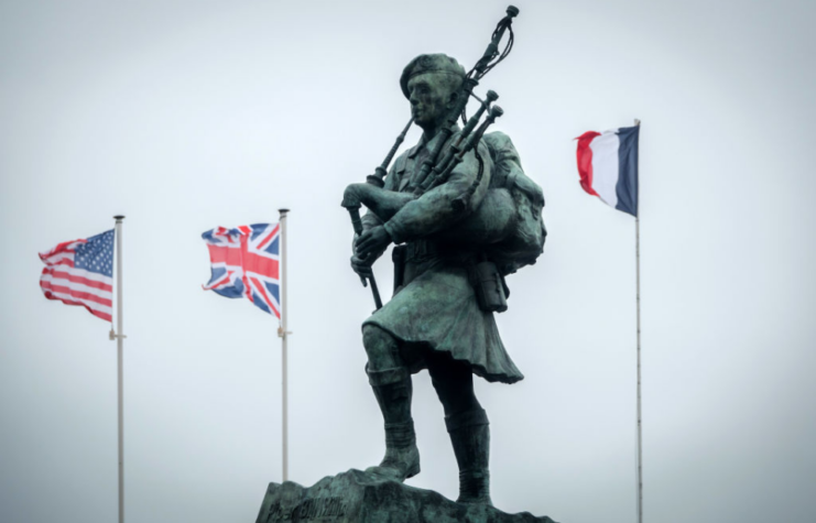 Flags flying around a statue of Bill Millin