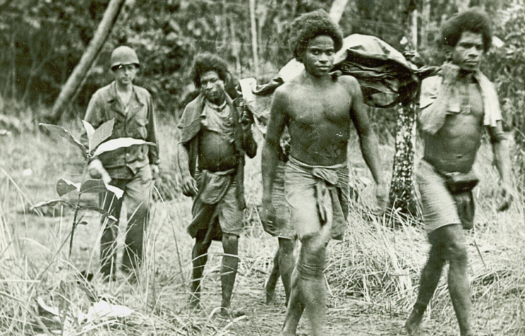 Fuzzy Wuzzy Angels carrying a stretcher while an Australian soldier follows behind