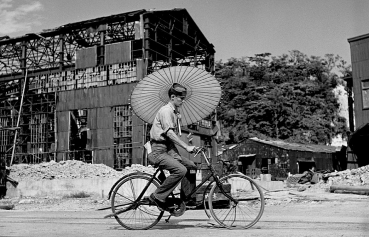 Man riding a bicycle while holding an umbrella