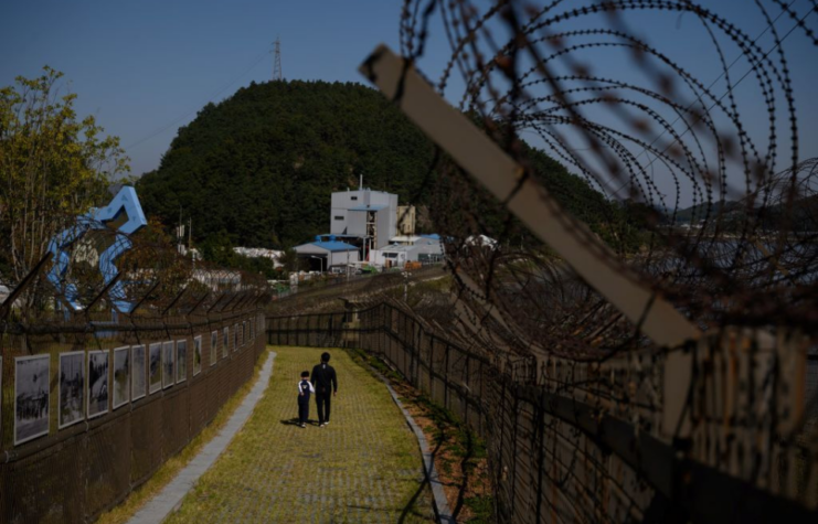 Man and child walking along the barbed wire fence of the Demilitarized Zone (DMZ) between North and South Korea