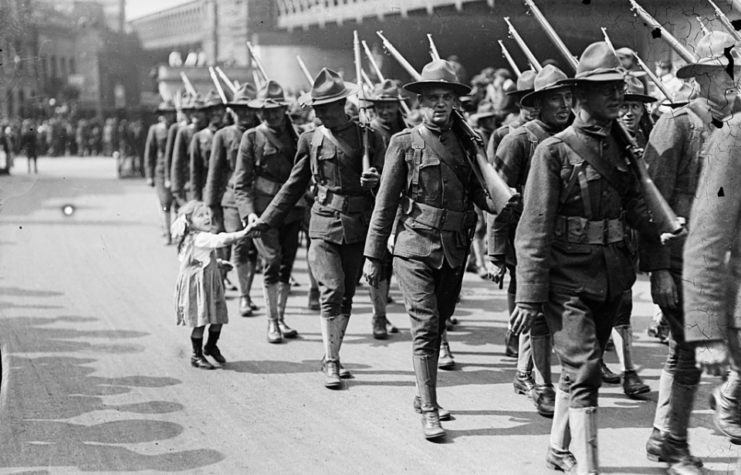 Young girl grabbing the hand of an American soldier while he marches with his comrades down a street