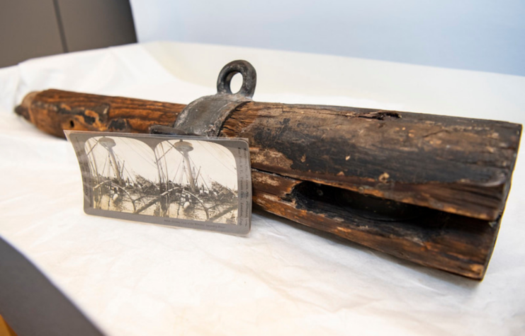 Wooden spar from the USS Maine (1889) on a white sheet with two photos of the ship's mast