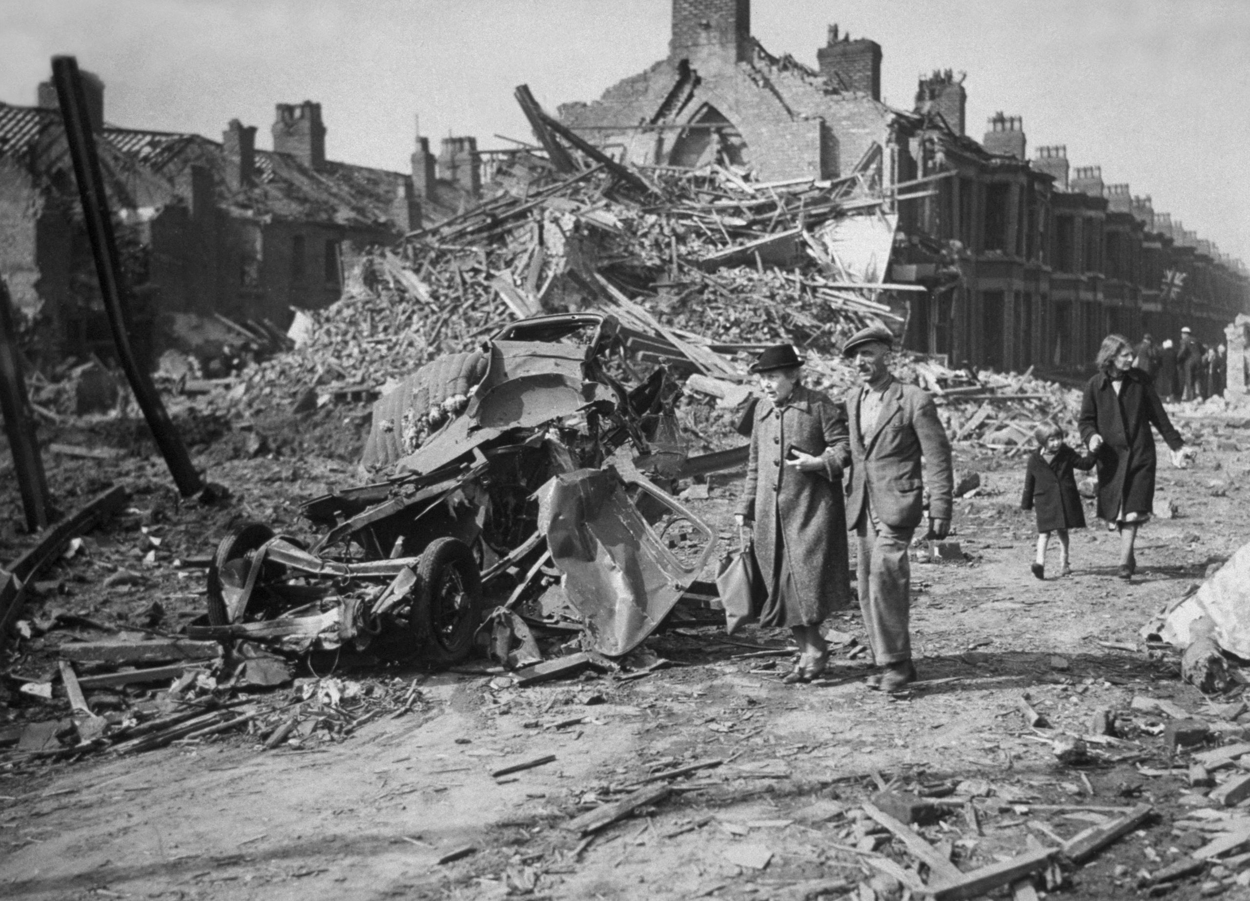 An elderly couple walking through a street with destroyed buildings.