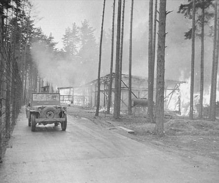 Black and white, car driving away from a building on fire, surrounded by trees. 