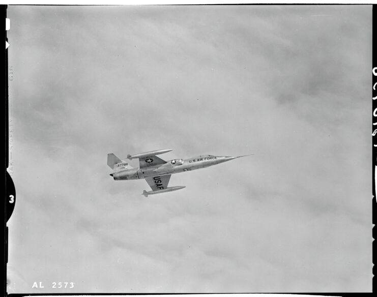 F-104 black and white, in flight in front of cloudy sky. image shot from below. 