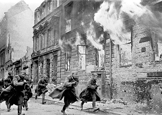 Red Army troops running past a burning building
