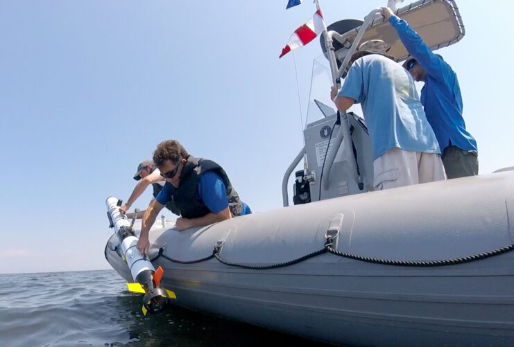 Crew in a small boat dropping a remotely operated vehicle (ROV) into the water