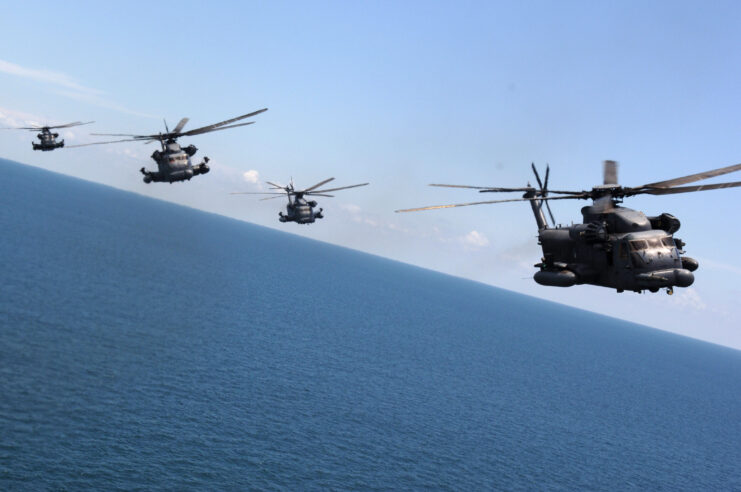 Front view of four gray MH-53 PAVE LOW helicopters flying over blue water. 