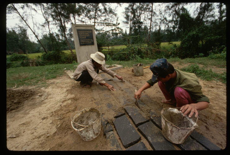 Two people crouch while doing repair work on the ground in front of the memorial in My Lai.