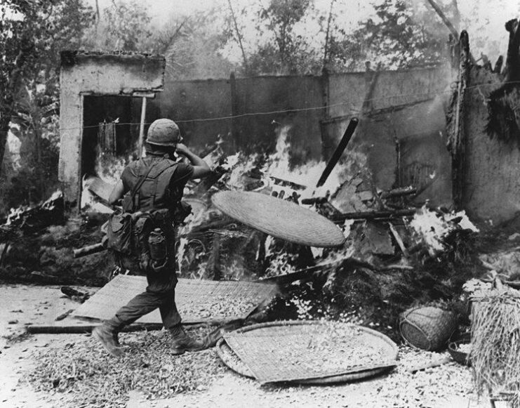 Black and white. SOldier taking a photograph of. a destroyed building. 