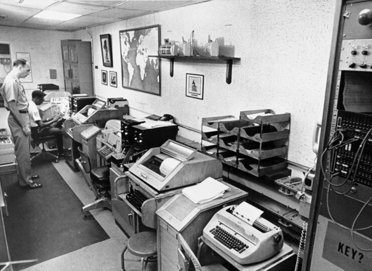 Man stands looking at a machine inside a room of the National Military Command Center. Black and white. 