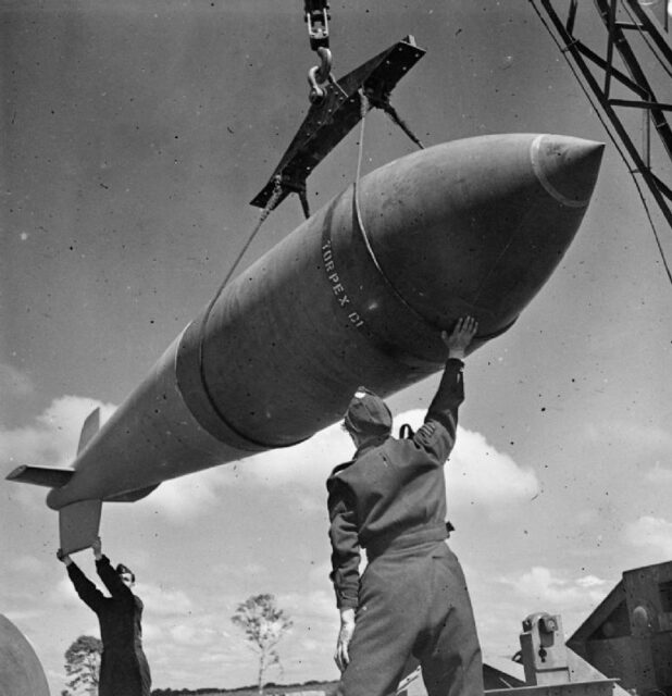 Royal Air Force (RAF) men standing beneath a "Tallboy" bomb that's being hoisted by a crane