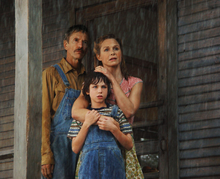 Movie still of a man, woman and boy in the rain from A Painted House (2003).