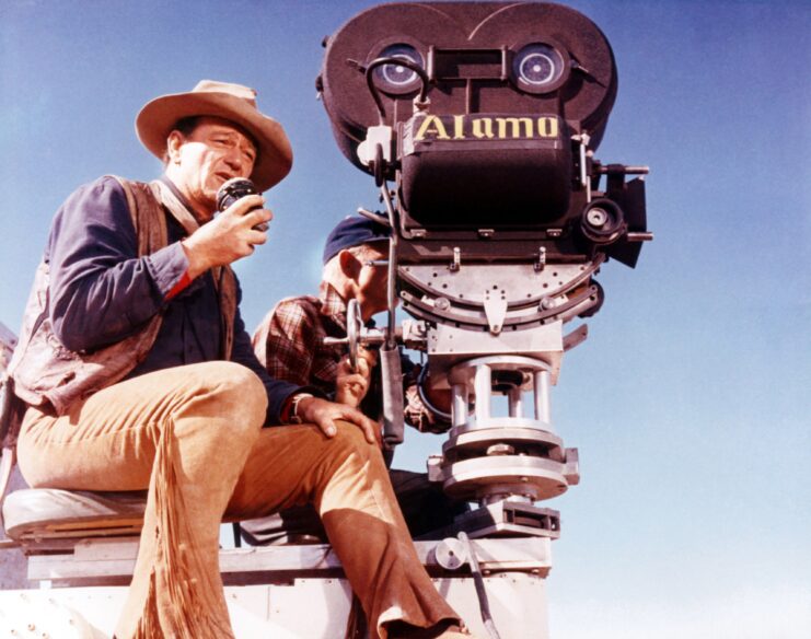 John Wayne sitting on the set of 'The Alamo' with a cameraman