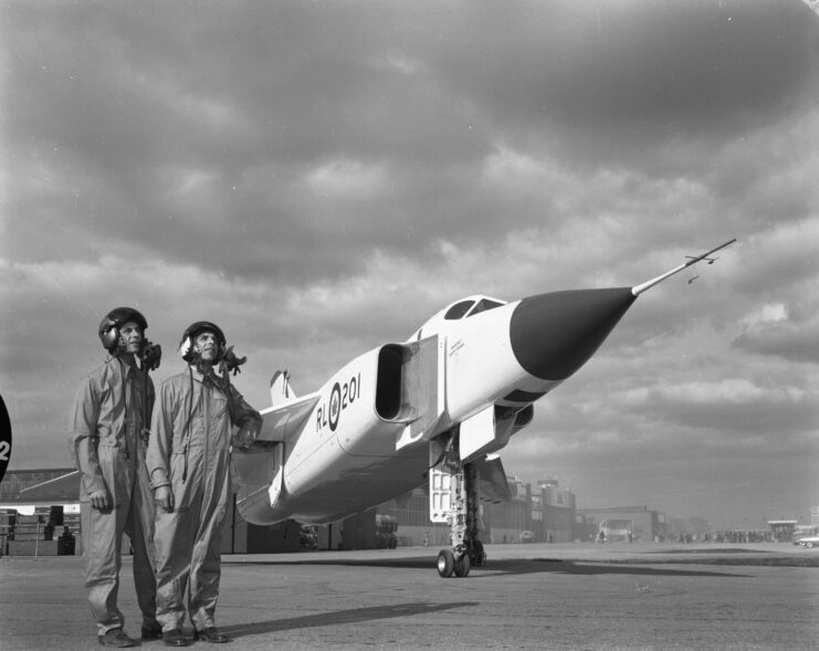 Black and white. Two men standing beside the Avro Arrow on a tarmac. 