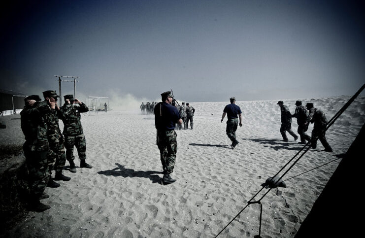 US Navy SEAL recruits running across a beach while superiors watch