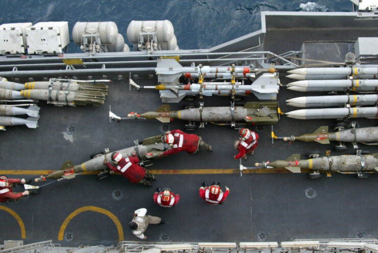 Overhead view of US Navy Ordnance handlers moving GBU-16 Paveway laser-guided bombs on the flight deck of the USS Kitty Hawk (CV-63)