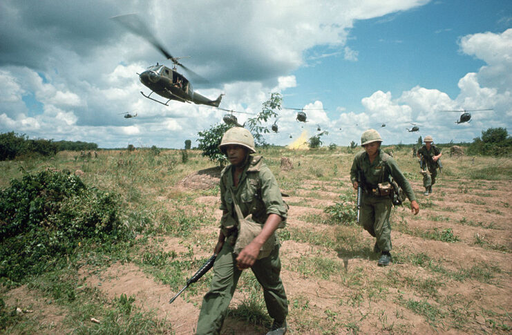 US infantrymen walking through a field while helicopters hover overhead