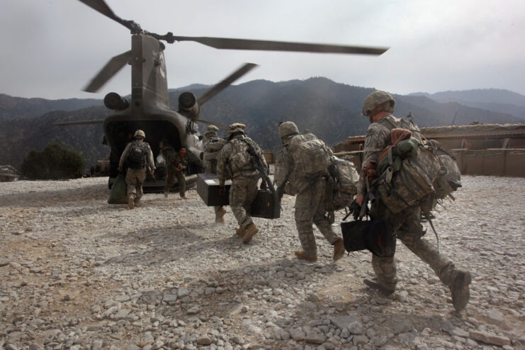 American soldiers running toward a Boeing CH-47 Chinook helicopter that's touched down in the middle of the desert