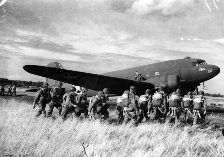 American paratroopers boarding a Douglas C-47 Skytrain that's parked in a grassy field